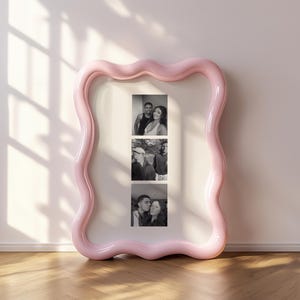 May include: A large, rectangular picture frame with a glossy, light pink, wavy, organic-shaped border. The frame contains a white mat board featuring three vertical black and white photographs of two individuals in various poses.