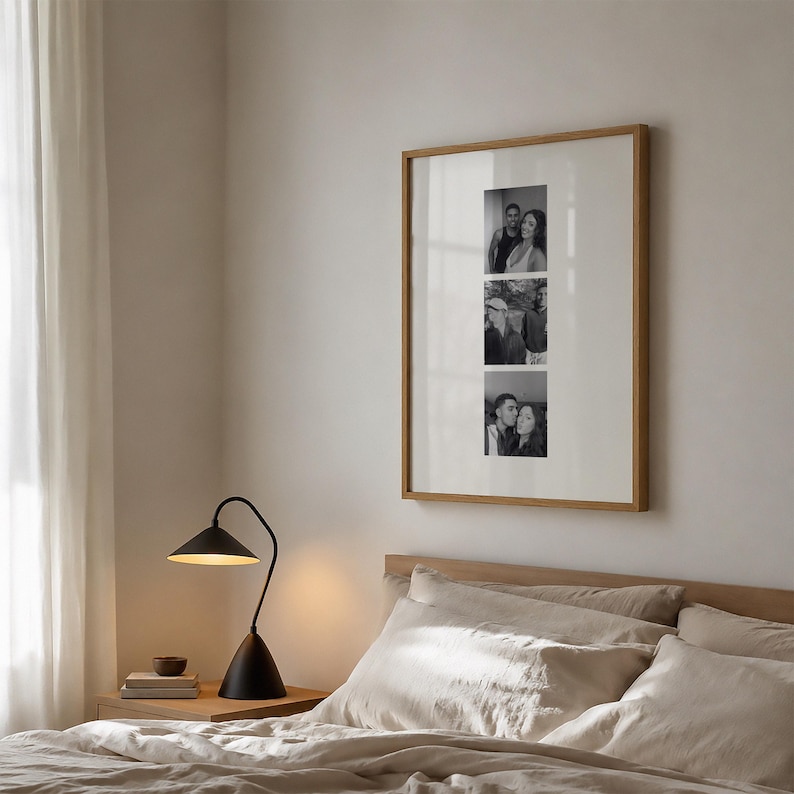 May include: A square wall art frame with a light wood finish containing a white mat and three vertical black and white photographs of people. The frame is displayed on a wall above a bed with beige bedding and a black desk lamp on a side table.