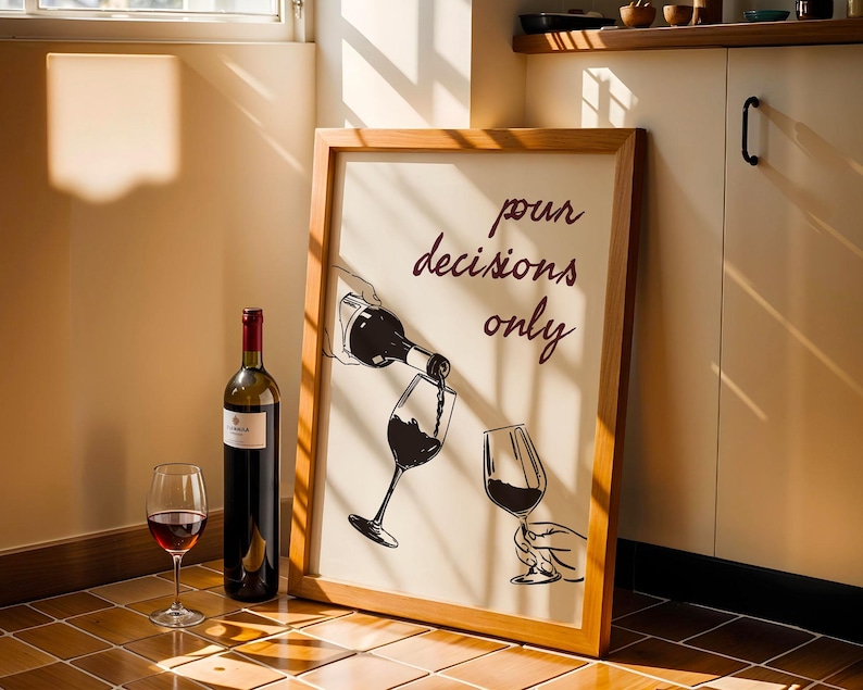 May include: A framed artwork with the text "pour decisions only" next to a wine bottle and a glass of red wine. The artwork depicts wine being poured into a glass. A full bottle of red wine and an empty wine glass are also present.