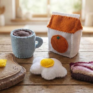 Może przedstawiać: Filcowy zestaw śniadaniowy, w tym niebieski kubek z kawą, tosty z masłem, jajko sadzone, paski bekonu i karton mleka z pomarańczą. Przedmioty są ułożone na drewnianej powierzchni.