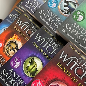 Op de afbeelding: Een verzameling paperbacks met een wolf op de omslag. De boeken zijn getiteld "The Witcher" en bevatten de naam van de auteur, Andrzej Sapkowski. De boeken zijn op elkaar gestapeld, met het bovenste boek "The Last Wish".