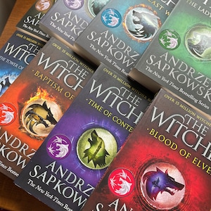 Op de afbeelding: Een stapel paperbacks met een fantasythema. De boeken zijn allemaal van Andrzej Sapkowski en tonen de Witcher-serie. De omslagen zijn een mix van rood, paars, blauw en zwart met wolvenbeelden.
