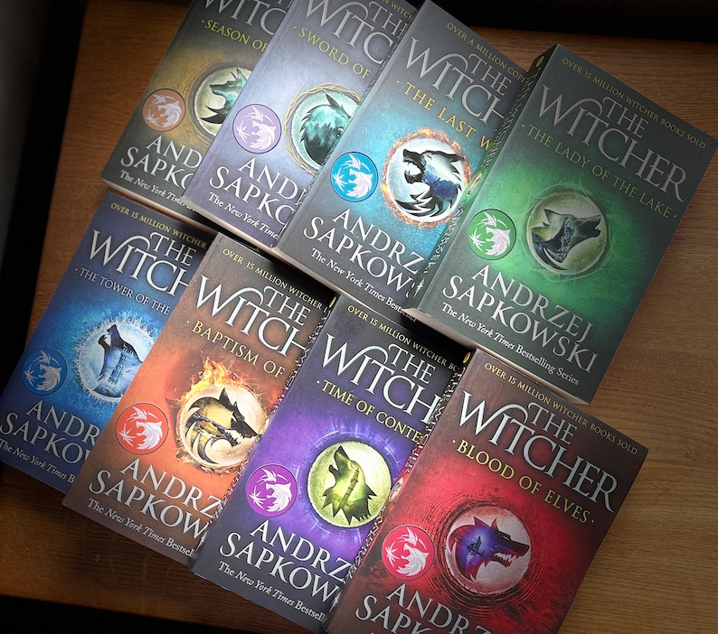 Op de afbeelding: Een verzameling van tien paperback boeken met groene, blauwe, rode, oranje en paarse omslagen. De boeken maken allemaal deel uit van de "The Witcher" serie van Andrzej Sapkowski. De omslagen bevatten een wolfskopf afbeelding en de titel "The Witcher".