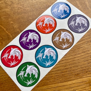 Op de afbeelding: Acht ronde stickers met een wit wolfskopontwerp met een vogel aan elke kant. De stickers zijn in verschillende kleuren, waaronder blauw, oranje, paars, bruin, rood, teal en groen.