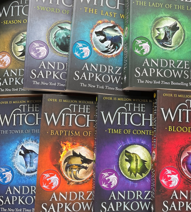 Op de afbeelding: Een verzameling van acht paperback boeken met kleurrijke omslagen met een wolf-afbeelding en de tekst "The Witcher" en "Andrzej Sapkowski".
