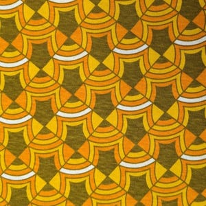 May include: Close-up of a fabric with a repeating geometric pattern. The design features a series of interlocking, fan-like shapes in shades of yellow, orange, and white against a dark olive-green background. The pattern creates a retro, textured appearance.