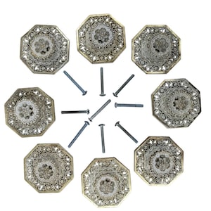 May include: A collection of eight octagonal cabinet knobs with ornate, filigree-style designs in silver and gold tones. Each knob features a central floral motif. Several silver screws are included.