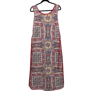 May include: Sleeveless maxi dress with a vibrant, geometric pattern in red, white, blue, and yellow. The dress features a scoop neckline and red trim along the edges. It hangs on a black hanger against a white background.
