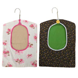 May include: Two fabric garment covers with hanger hooks. One is white with pink floral print and a pink trim around the oval opening. The other is dark brown with a floral pattern and a green interior. Both have a button closure.