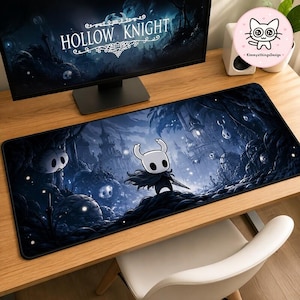 Op de afbeelding: Een rechthoekige bureaumat met een donkere, sfeervolle illustratie uit het videospel Hollow Knight. Het ontwerp toont een klein, wit, gehoornd personage dat een spijker vasthoudt, tegen een achtergrond van blauwachtige ruïnes en gebladerte.