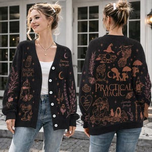 Könnte beinhalten: Eine schwarze Strickjacke mit V-Ausschnitt, Knopfleiste und langen Ärmeln. Das Kleidungsstück ist mit kupferfarbenen Strichzeichnungen magischer Motive verziert, darunter ein Kessel, ein Mond und der Schriftzug Practical Magic und Rosemary by the gate.