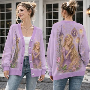 May include: A light purple knit cardigan featuring a graphic of a long-haired character with a small green lizard. The back displays a tall tower, floating lanterns, and a framed silhouette. The front includes a button closure and ribbed trim.