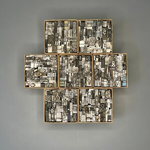 May include: A collection of vintage metal letterpress printing blocks in various sizes and styles, arranged in a grid pattern. The blocks are made of lead and contain a variety of letters, numbers, and symbols.