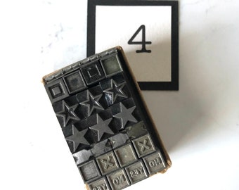May include: A vintage metal printing block set with a variety of characters and symbols, including stars, squares, and the words "yes", "no", and "say". The set is arranged in a rectangular box with a brown paper exterior.