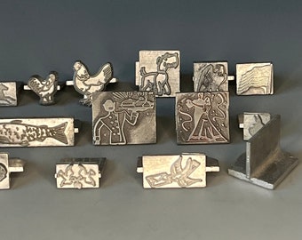 May include: A collection of 12 vintage metal printing blocks, featuring various designs including a chicken, a dog, a fish, a chef, and a bird. The blocks are made of metal and have a worn, antique look.