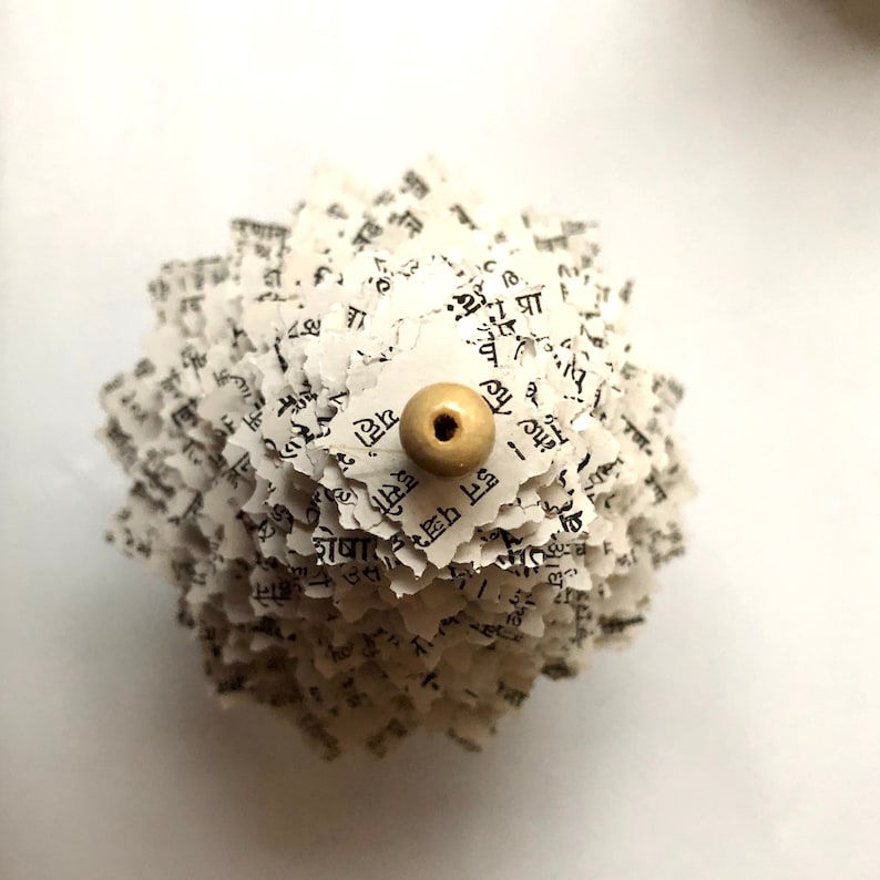 May include: A white paper flower made from pages of a book with a beige bead in the centre.
