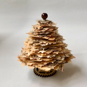 May include: A small, decorative Christmas tree made from pages of an old book. The tree is topped with a wooden ball and sits on a wooden gear base.