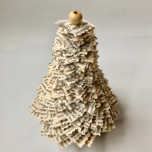 May include: A small, white, paper Christmas tree made from pages of a book. The tree is decorated with a small, white bead at the top.