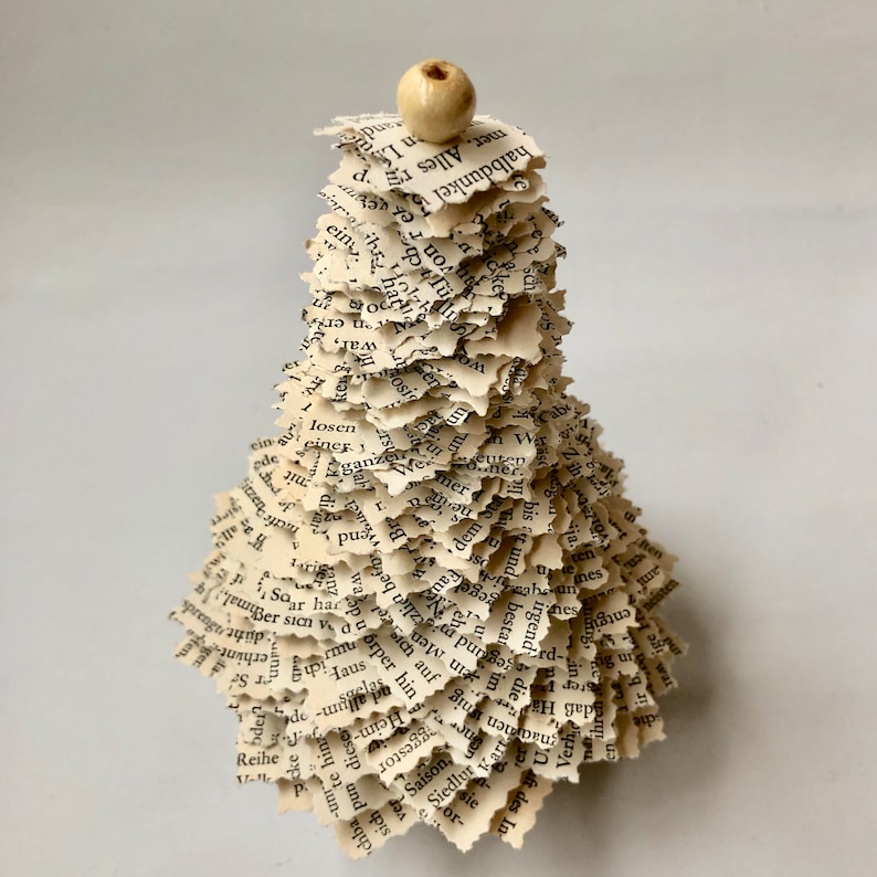 May include: A small, white, paper Christmas tree made from pages of a book. The tree is decorated with a small, white bead at the top.