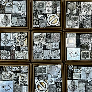 May include: Nine square boxes filled with vintage metal printing blocks. The blocks feature various designs, including a smiley face, an anchor, a hot air balloon, and a no symbol. The blocks are arranged in a grid pattern.
