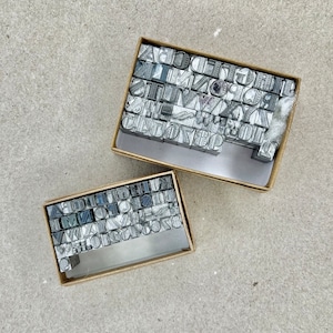 May include: Two boxes filled with letterpress printing blocks. The blocks are made of metal and have letters and symbols on them. The boxes are made of cardboard and have a brown color.