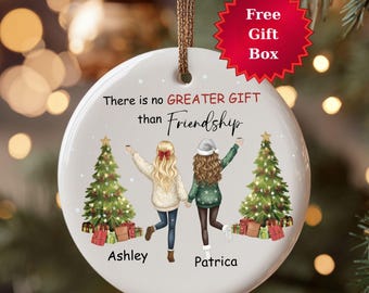 May include: A round ceramic Christmas ornament with a friendship theme. It features two illustrated figures, Christmas trees, and the text "There is no GREATER GIFT than Friendship." The ornament has a brown string for hanging and a red starburst that says "Free Gift Box."