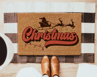 Könnte beinhalten: Eine rechteckige Fußmatte mit Weihnachtsmotiv. Die Matte zeigt einen Weihnachtsmann in einem von Rentieren gezogenen Schlitten mit dem Wort "Christmas" in einer Retro-Schriftart. Die Matte ist braun mit einem karierten Rand.