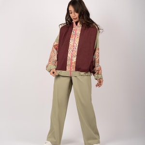 Könnte beinhalten: Ein olivgrüner Trainingsanzug. Die Jacke hat eine weinrote Mittelbahn mit einem bunten Blumenmuster und einem rosa Reißverschluss. Die Ärmel und Seiten der Jacke sind olivgrün. Die Hose ist weit geschnitten und olivgrün. Die Person trägt weiße Turnschuhe.