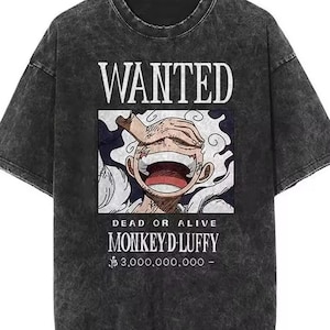 May include: Dark grey t-shirt featuring a graphic of a smiling character with the text "WANTED" above and "MONKEY D LUFFY" below. The shirt also features the text "DEAD OR ALIVE" and a monetary value. The t-shirt has a vintage, washed appearance.