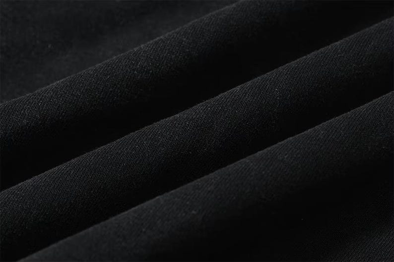 May include: Close-up of black fabric with visible texture and folds. The material appears to be a dark, solid color, possibly cotton or a similar textile. The image highlights the fabric's texture and the way it drapes.