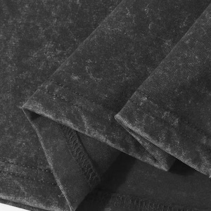 May include: Close-up of a dark gray t-shirt with a textured, acid-wash effect. The fabric is folded, revealing the hem and seams. The shirt appears to be made of a soft, comfortable material.
