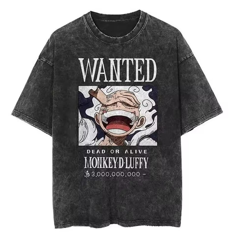 May include: Dark grey t-shirt featuring a graphic of a smiling character with the text "WANTED" above and "MONKEY D LUFFY" below. The shirt also features the text "DEAD OR ALIVE" and a monetary value. The t-shirt has a vintage, washed appearance.