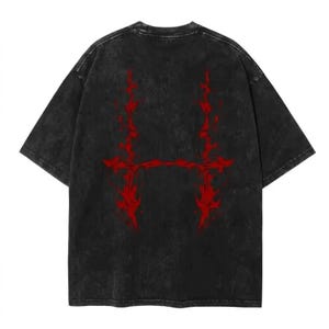 May include: A black, oversized t-shirt with a distressed, vintage wash. The back of the shirt features a bold, red graphic design. The graphic is a stylized, symmetrical design with a horizontal bar connecting two vertical flame-like elements.