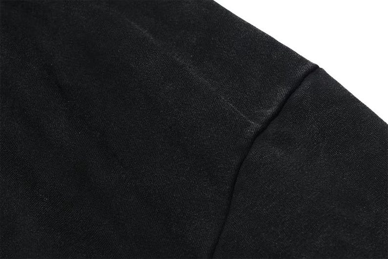 May include: Close-up of a black fabric, possibly a garment. The material appears to be textured, with visible seams. The image highlights the details of the textile, showcasing its color and construction.