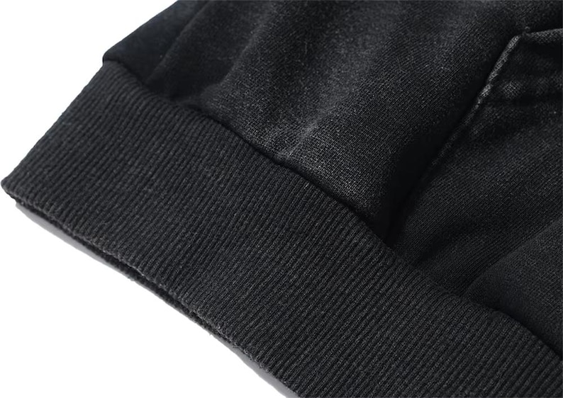 May include: Close-up of a black garment, possibly a sweatshirt or hoodie, with a ribbed cuff. The fabric appears to be a soft, textured material. The image highlights the details of the fabric and construction.