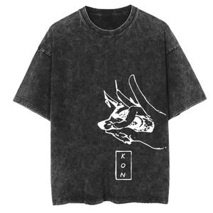 May include: Dark gray t-shirt with a white graphic of a hand and a stylized animal head. The shirt has a vintage, acid-wash look. The text "KON" is printed vertically in a white rectangle.