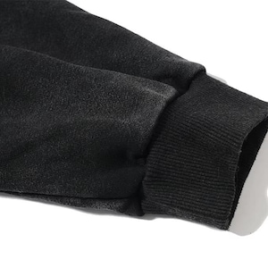 May include: Close-up of a black sweatshirt sleeve. The cuff is ribbed and dark, contrasting with the lighter background. The fabric appears to be a soft, textured material.
