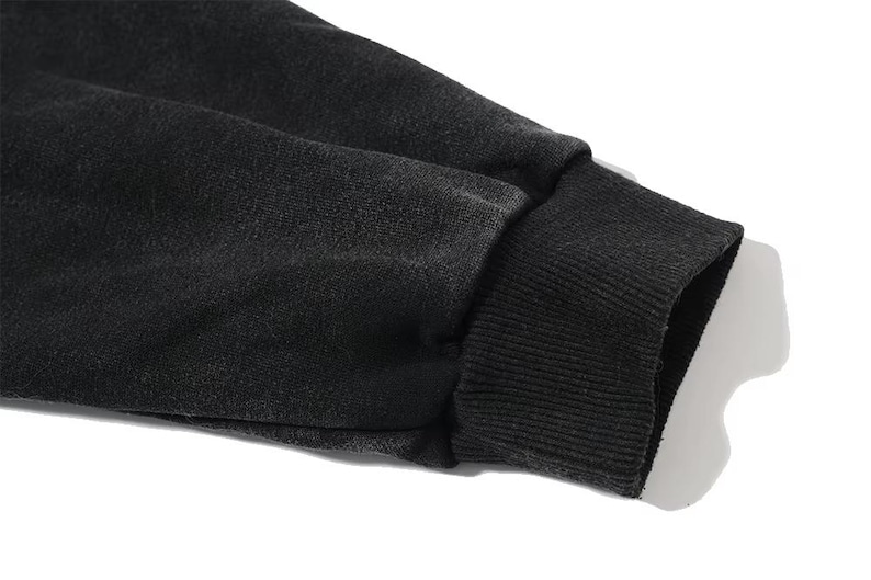 May include: Close-up of a black sweatshirt sleeve. The cuff is ribbed and dark, contrasting with the lighter background. The fabric appears to be a soft, textured material.