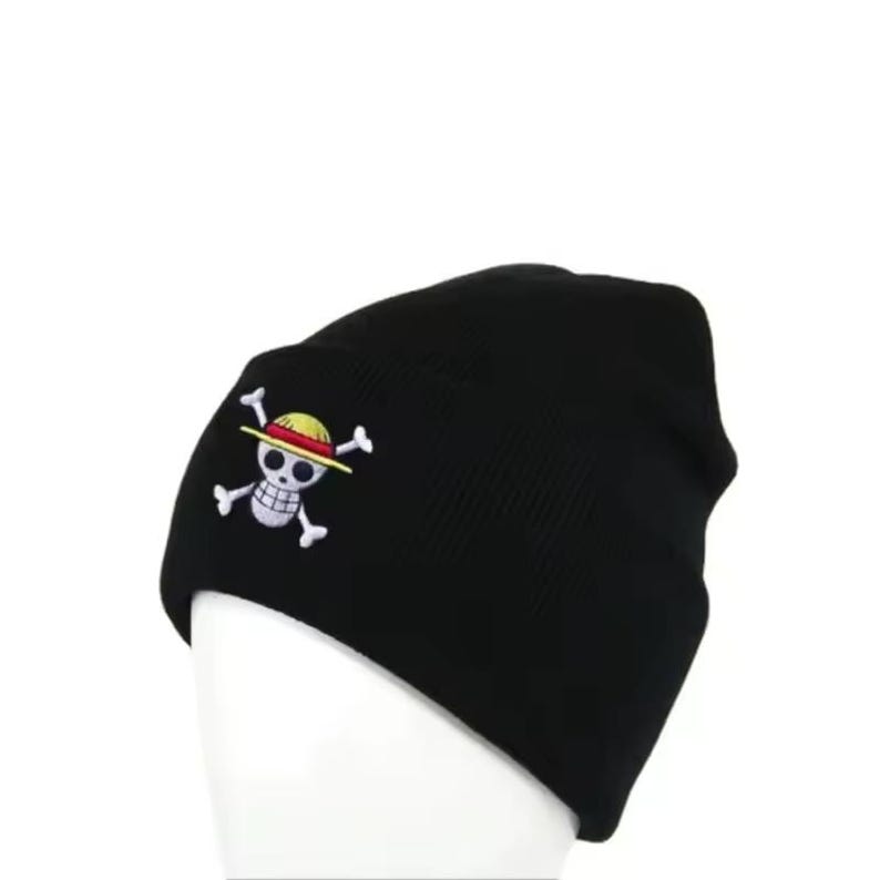 May include: Black beanie hat with a white skull and crossbones logo featuring a yellow straw hat. The logo is embroidered on the front of the hat. The hat is made of a soft, knitted material.