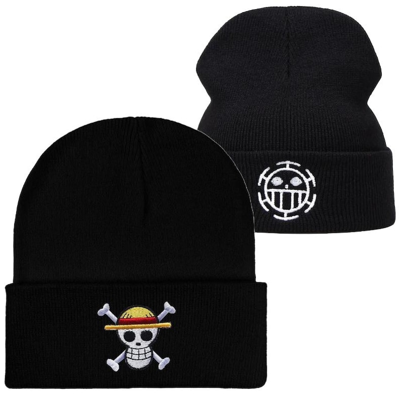 May include: Black knit beanie hats with embroidered designs. One hat features a skull and crossbones with a straw hat, while the other displays a white circular emblem. The hats are made of a soft, ribbed knit material.