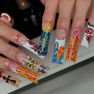 May include: Long, acrylic nails with various designs. One nail features a tiger, another has a koi fish, and others display roses and text. The nails have a clear base with colorful artwork.