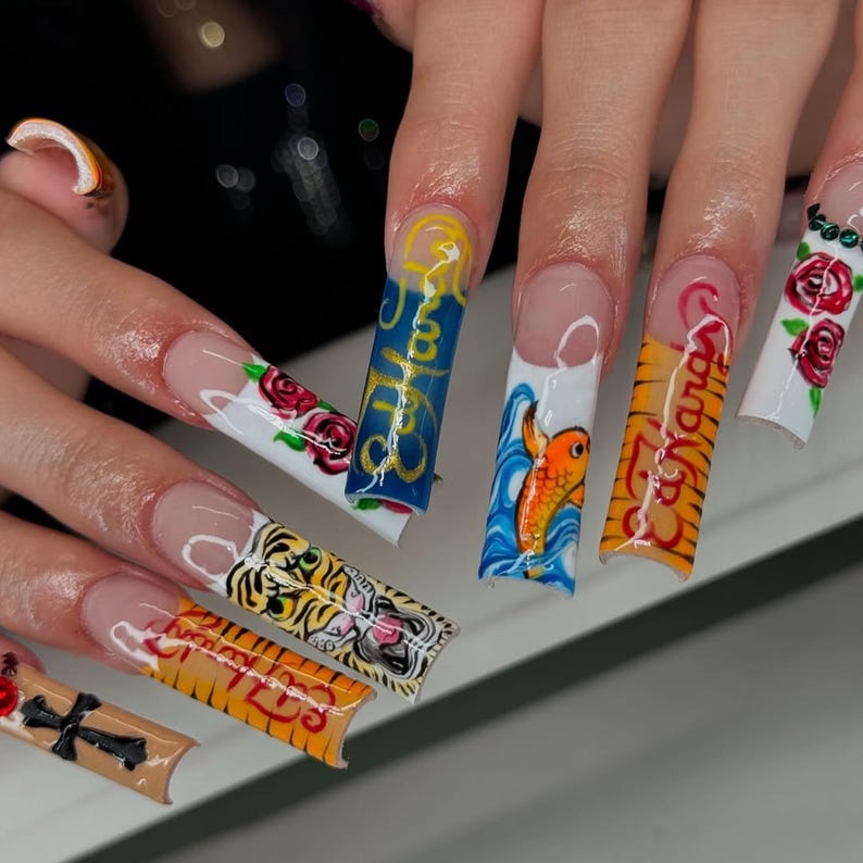 May include: Long, acrylic nails with various designs. One nail features a tiger, another has a koi fish, and others display roses and text. The nails have a clear base with colorful artwork.