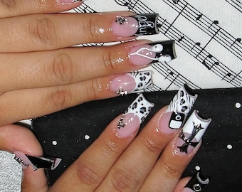 May include: A set of long, acrylic nails with various designs. Some nails feature a pink base with black and white cow print tips. Others have black tips with silver embellishments and the word "Angel".