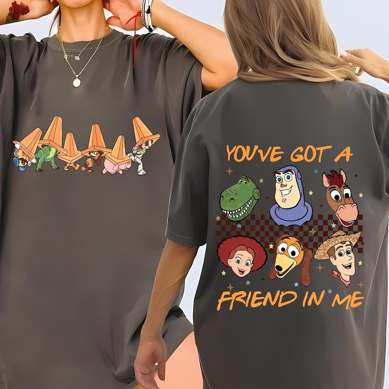 May include: Dark gray t-shirt featuring cartoon characters from Toy Story. The front of the shirt shows characters wearing orange traffic cones. The back of the shirt has the phrase "YOU'VE GOT A FRIEND IN ME" with character illustrations.