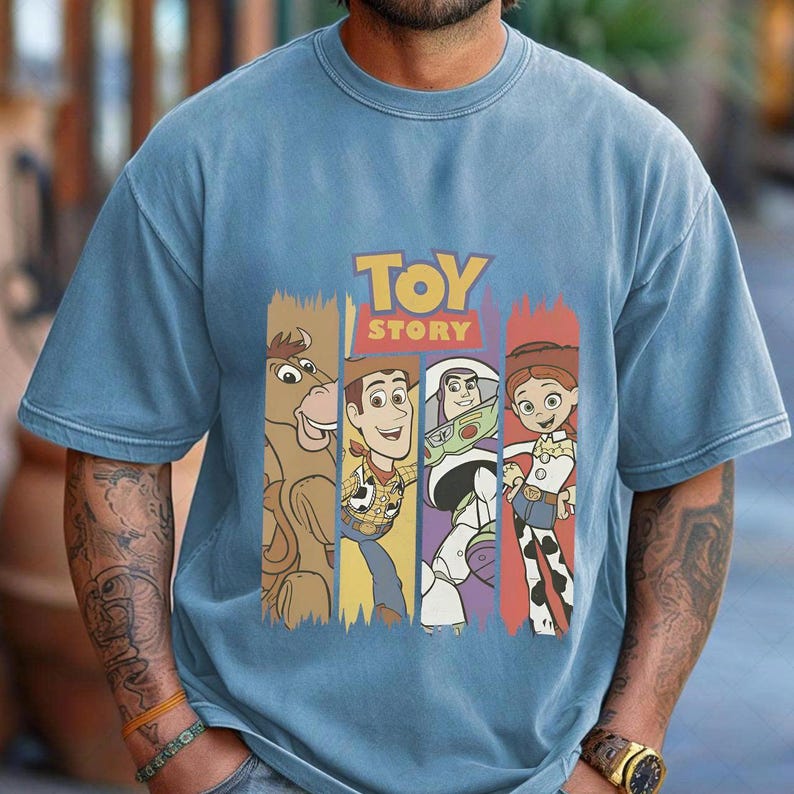 May include: A pale blue t-shirt with the words "TOY STORY" in yellow and red. The shirt features cartoon characters from the film, including Woody, Buzz Lightyear, and Jessie, each in a vertical colour block.