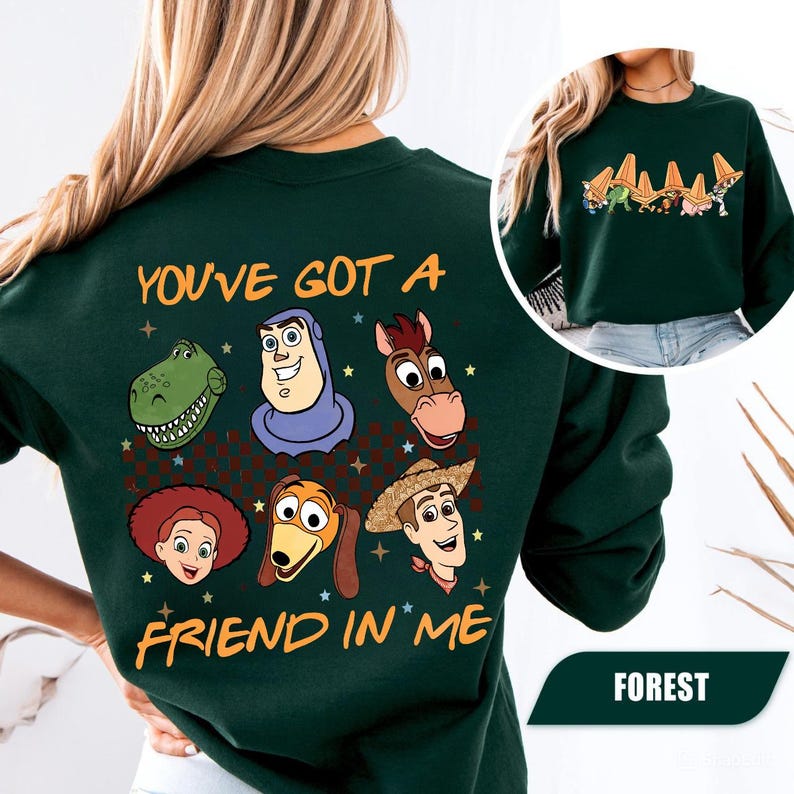 May include: Forest green sweatshirt featuring cartoon character graphics and the text "YOU'VE GOT A FRIEND IN ME". The design includes images of a dinosaur, Buzz Lightyear, a horse, Jessie, Slinky Dog, and Woody.