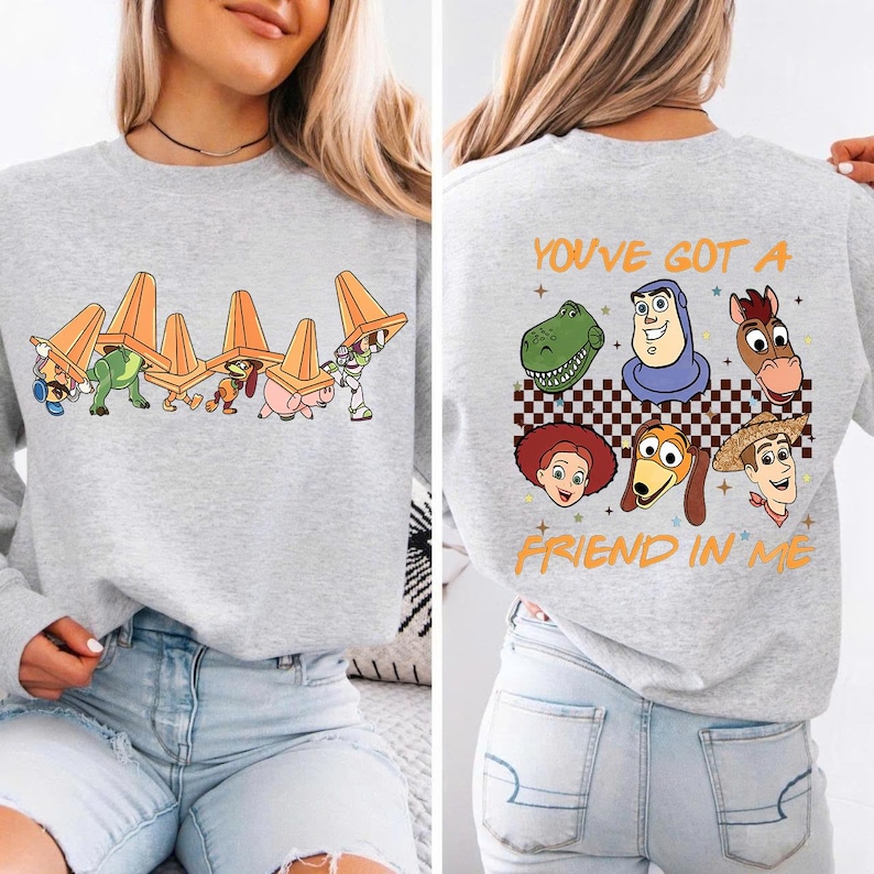 May include: A light gray sweatshirt featuring a colorful graphic of characters from a popular animated film. The front design shows characters carrying orange traffic cones. The back of the sweatshirt has the text "YOU'VE GOT A FRIEND IN ME" with character faces.