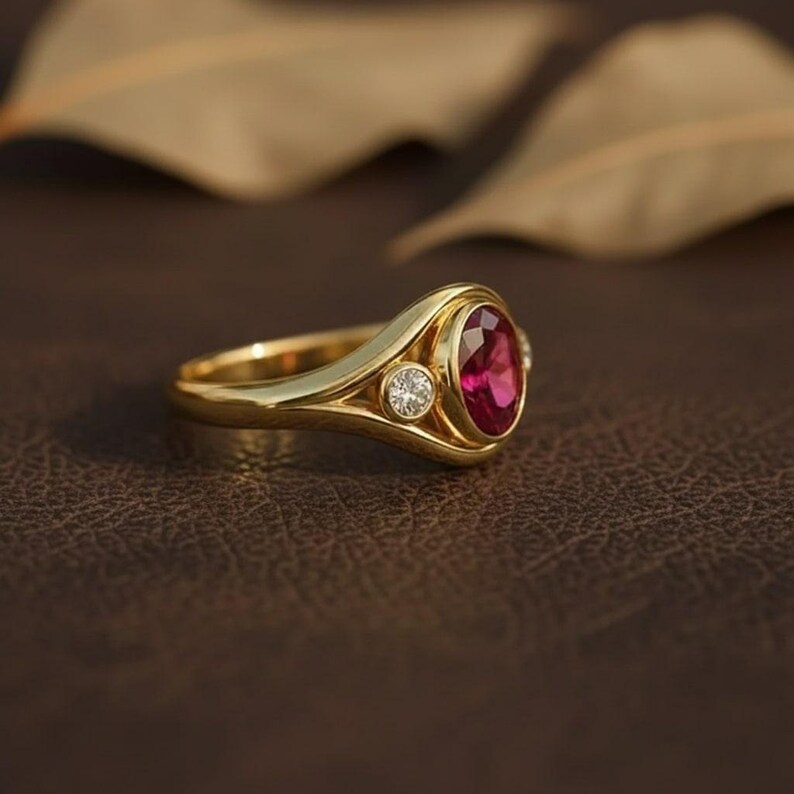 Puede incluir: Un anillo de oro con un gran rub&iacute; ovalado y dos peque&ntilde;os diamantes. El anillo tiene una banda pulida y un dise&ntilde;o cl&aacute;sico. El rub&iacute; es de color rojo intenso y los diamantes brillan. Una hermosa joya.