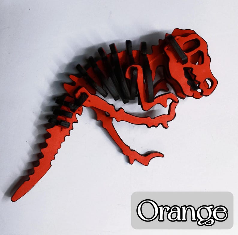 May include: An orange wooden dinosaur skeleton puzzle with black accents. The dinosaur has a detailed skeletal structure and is lying down. The word "Orange" is written in a white font on a gray rectangle.