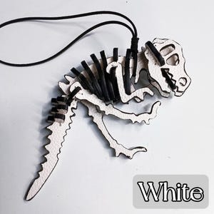 May include: White dinosaur skeleton pendant with black accents and a black cord. The pendant features a detailed design of a dinosaur skeleton, with the word "White" in a gray rectangle.